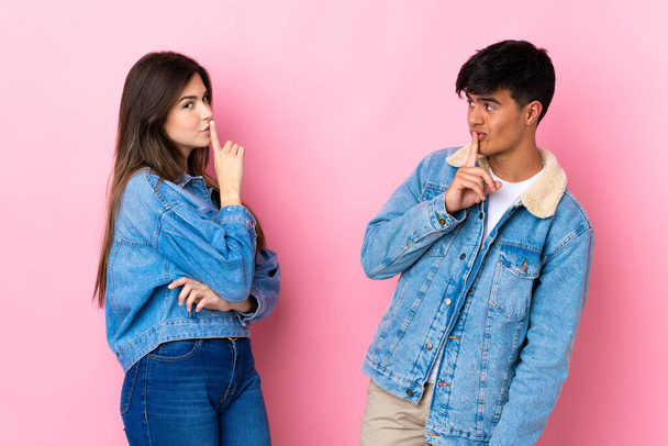 Young couple over isolated pink background showing a sign of closing mouth and silence gesture - Photo, Image