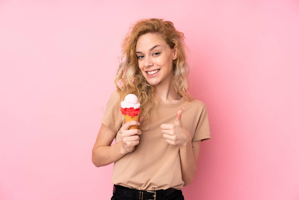 Jovem loira segurando um sorvete de corneto isolado no fundo rosa com os polegares para cima, porque algo bom aconteceu - Foto, Imagem
