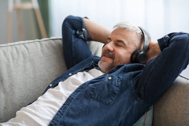 Boldog felnőtt férfi feküdt a kanapén, zenét hallgatva - Fotó, kép