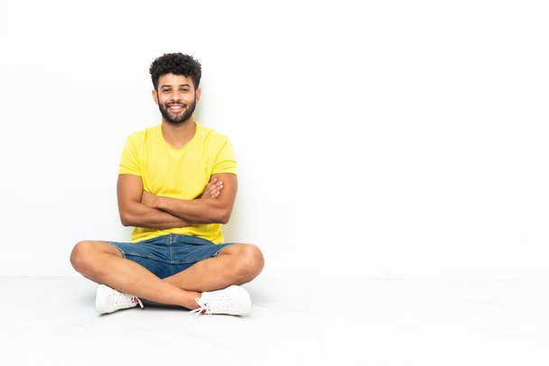 Jovem marroquino bonito homem sentado no chão sobre fundo isolado mantendo os braços cruzados na posição frontal - Foto, Imagem