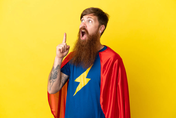 Redhead Super Hero man isolated on yellow background thinking an idea pointing the finger up - Photo, Image