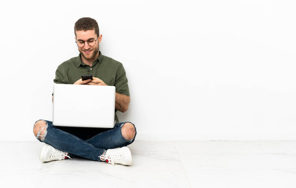 Молодий чоловік сидить на підлозі, надсилаючи повідомлення з мобільним
 - Фото, зображення
