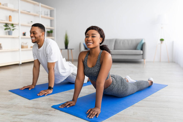 Cool coppia nera facendo posa cobra sul tappetino yoga in soggiorno. Soggiorno a casa attività concetto - Foto, immagini