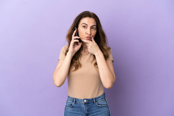 Middle aged caucasian woman using mobile phone isolated on purple background thinking - Zdjęcie, obraz