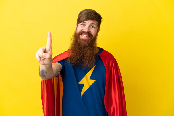 Redhead Super Hero man isolated on yellow background showing and lifting a finger - Photo, Image