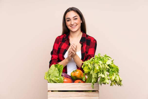 Fermier avec des légumes fraîchement cueillis dans une boîte isolée sur fond beige applaudissant - Photo, image
