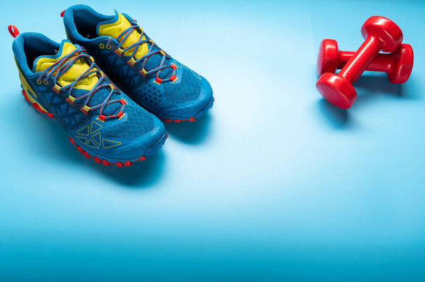 Μπλε εκπαιδευτές και κόκκινα βαράκια για φυσική κατάσταση. Αθλητικά αθλητικά παπούτσια σε μπλε φόντο. Γυμναστική. - Φωτογραφία, εικόνα