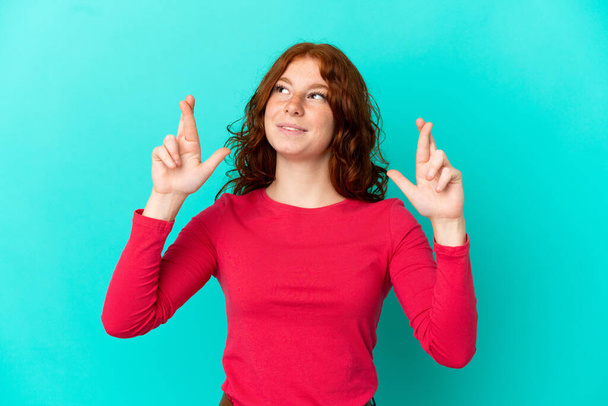 Teenager reddish woman isolated on blue background with fingers crossing and wishing the best - Fotoğraf, Görsel