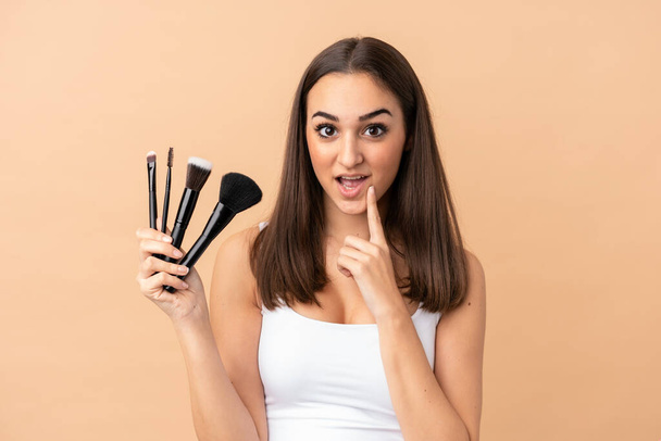 Jeune femme caucasienne isolée sur fond beige tenant la brosse de maquillage - Photo, image