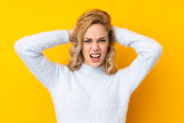 Young blonde woman isolated on yellow background frustrated and takes hands on head - Photo, Image