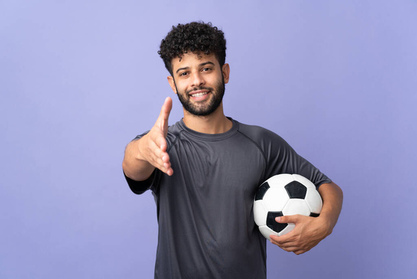 Bonito marroquino jovem jogador de futebol homem sobre isolado no fundo roxo apertando as mãos para fechar um bom negócio - Foto, Imagem