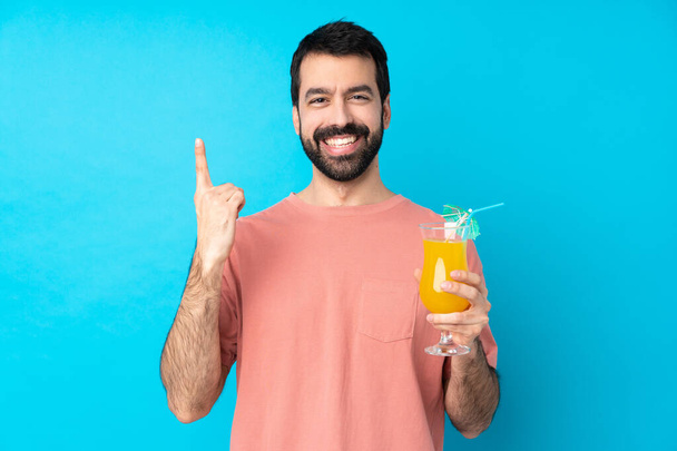 Young man over holding a cocktail over isolated blue background pointing up a great idea - Zdjęcie, obraz