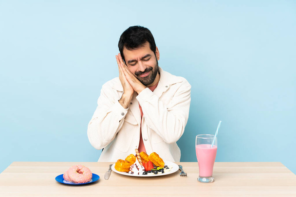 Чоловік за столом сніданок вафлі і молочний коктейль робить жест сну в недоступному виразі
 - Фото, зображення