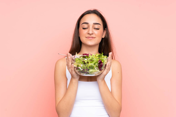 jonge Kaukasische vrouw houden een salade geïsoleerd op roze achtergrond - Foto, afbeelding