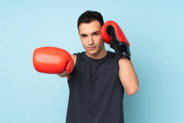Mavi arka planda, boks eldivenleriyle izole edilmiş genç bir sporcu. - Fotoğraf, Görsel