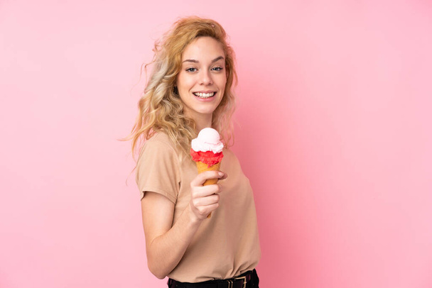 Young blonde woman holding a cornet ice cream isolated on pink background with happy expression - Foto, imagen