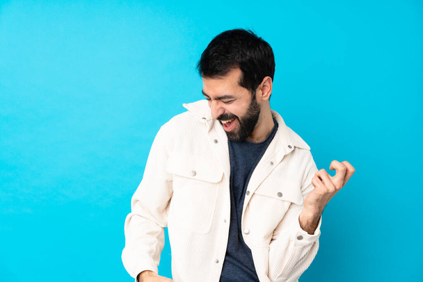Young handsome man with white corduroy jacket over isolated blue background making guitar gesture - Фото, зображення