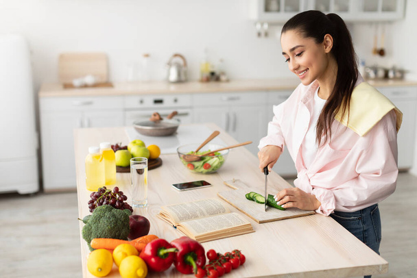 Frau kocht Salat und verwendet Kochbuch in der Küche - Foto, Bild