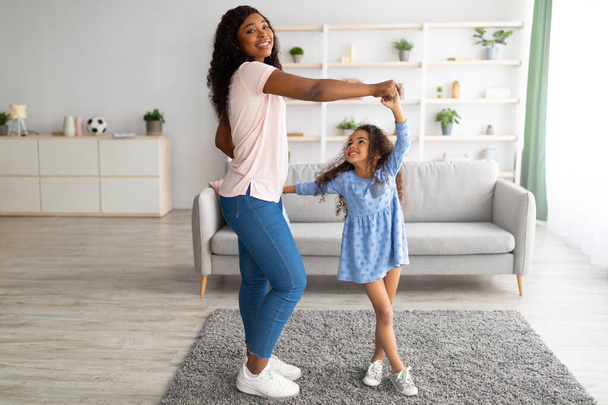 Afroamerikanische Mutter tanzt zu Musik mit ihrer süßen kleinen Tochter zu Hause - Foto, Bild