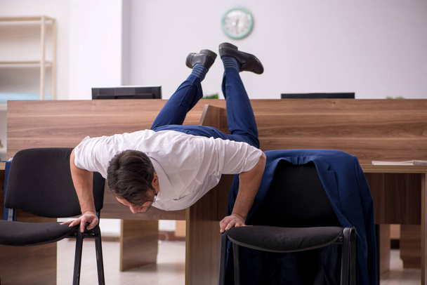 Young businessman employee doing sport exercises at workplace - Fotoğraf, Görsel
