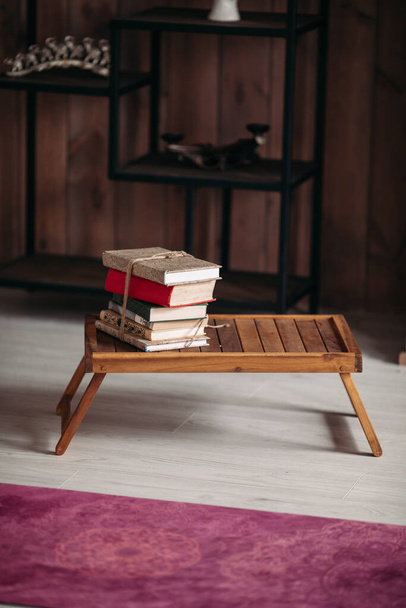 Bild eines Bücherstapels auf einem kleinen Holztisch im hellen Raum - Foto, Bild