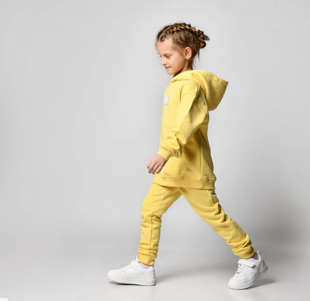 Full portrait of a young beautiful girl with stylish haircut in yellow modern tones, with a hoodie sweatshirt, walking, waving her arms outstretched - Foto, Bild