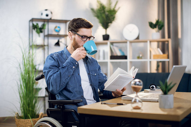 Handicapped freelancer drinking coffee and reading book - Фото, зображення