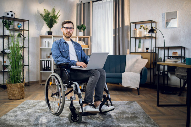 Nuori mies freelancer istuu pyörätuolissa ja käyttää kannettavaa - Valokuva, kuva