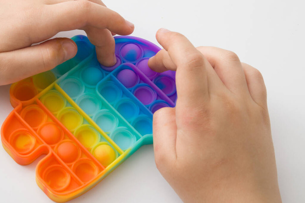 Primo piano mani per bambini con giocattolo in silicone arcobaleno antistress pop it, vista dall'alto su sfondo bianco. Giocattolo popolare per bambini - Foto, immagini