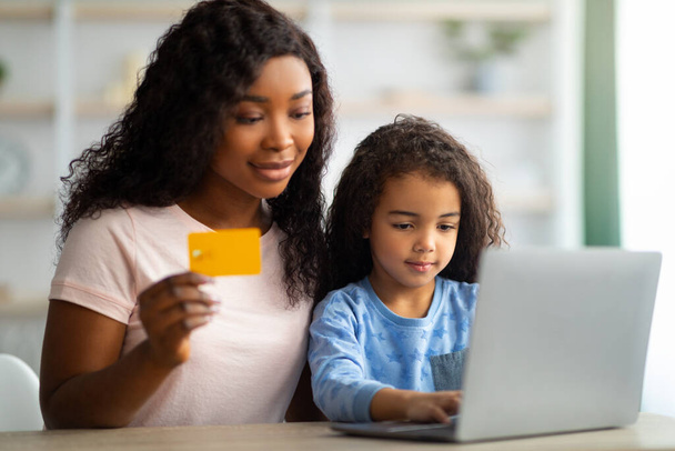 Afroamerykańska matka robi zakupy online z kartą kredytową, dokonując zakupów w Internecie z córką z domu - Zdjęcie, obraz