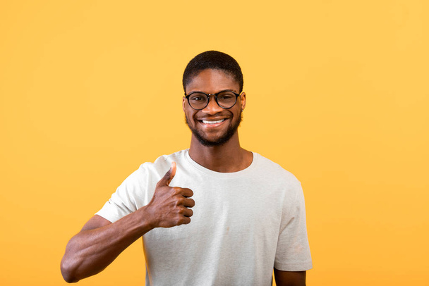 I like it. Joyful black man gesturing thumb up, approving and recommending something over yellow background, studio shot - Фото, изображение