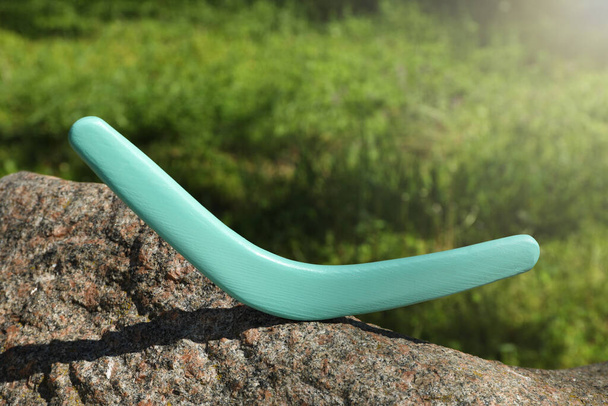 Sunlit turquoise wooden boomerang on stone outdoors - Fotó, kép