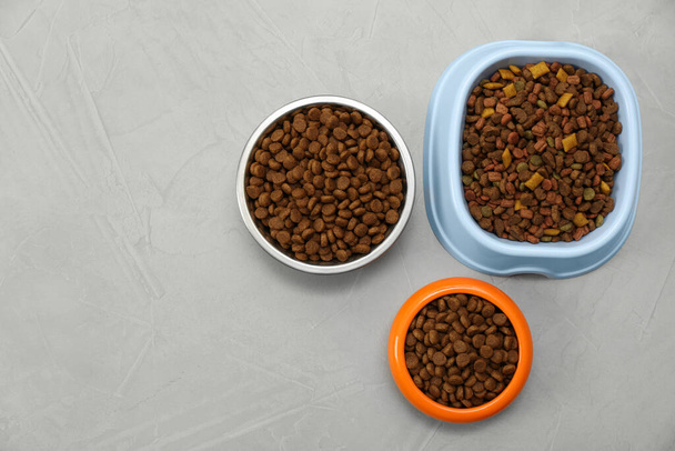 Dry food in pet bowls on grey background, flat lay. Space for text - Fotoğraf, Görsel
