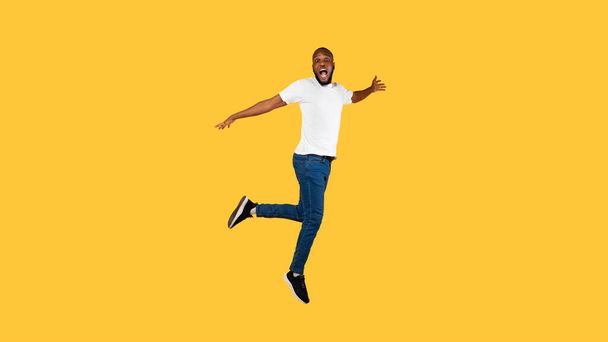 Приголомшений афро - американський хлопець, який робить стрибки, дивлячись у камеру, жовте тло - Фото, зображення