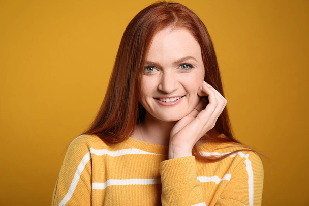 Candid portrait of happy young woman with charming smile and gorgeous red hair on yellow background - Valokuva, kuva