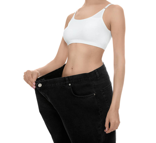 Mujer joven con pantalones vaqueros grandes después de la pérdida de peso sobre fondo blanco, primer plano - Foto, Imagen