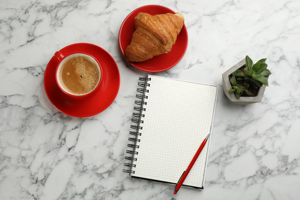 Notebook, cup of aromatic coffee, delicious croissant and plant on white marble table, flat lay - Foto, Bild