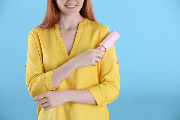 Young woman cleaning clothes with lint roller on light blue background, closeup - Fotó, kép