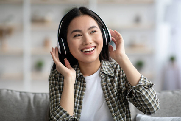 Happy young asian woman in wireless headphones enjoying music - Фото, зображення