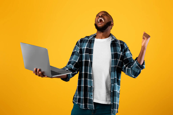 Overjoyed afroamericano uomo holding laptop gesturing sì, sfondo giallo - Foto, immagini