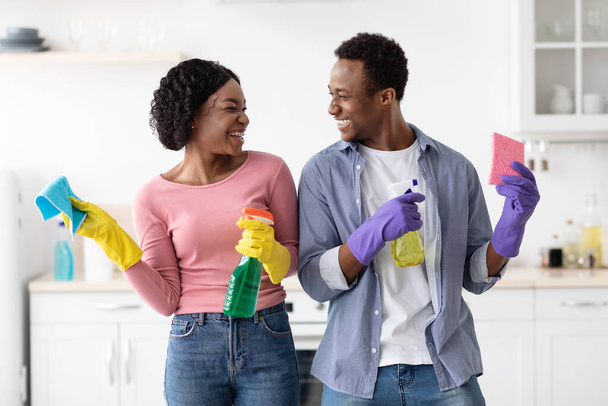 Sorrindo casal preto com suprimentos para limpeza posando na cozinha - Foto, Imagem