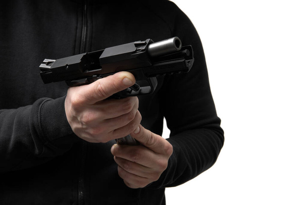 A man in dark clothes holds a pistol in his hands and reloads it. Unloaded weapon in hand. - Photo, image