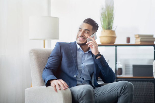 Арабский бизнесмен разговаривает по мобильному телефону в офисе, сидит в кресле, разговаривает с другом или клиентом - Фото, изображение