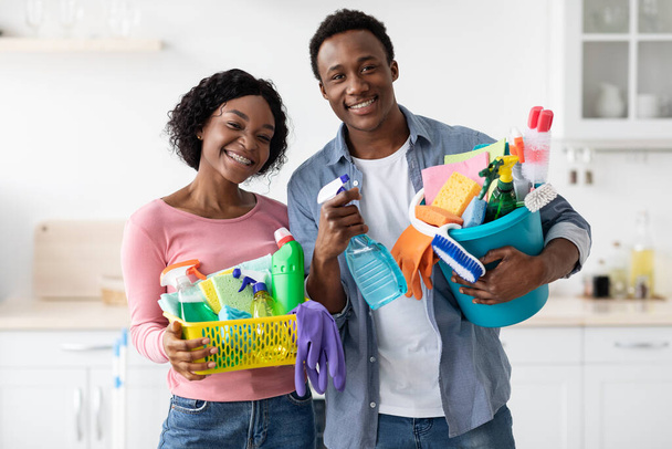Positive black couple with cleaning tools posing in kitchen - Фото, изображение