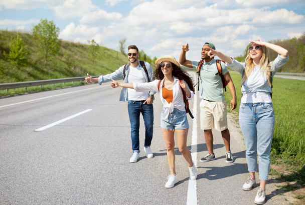 Group of young people standing on roadside, stopping car with hitchhiking gestures, having fun road trip, copy space - Foto, Imagen