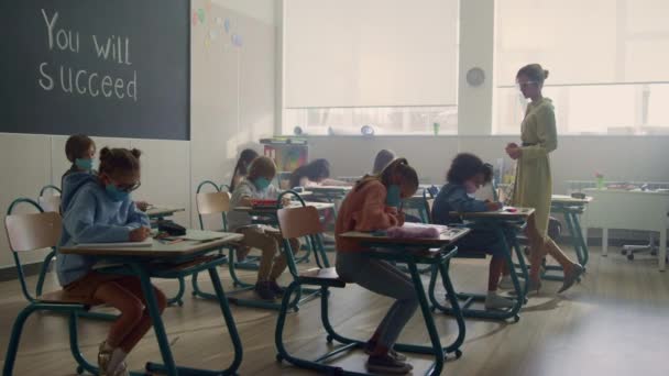 Bambini in maschere mediche che studiano insieme in classe durante la pandemia di coronavirus - Filmati, video