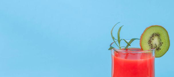 Cocktail rosso con kiwi e rosmarino a destra su sfondo azzurro con spazio per il testo a sinistra, vista da vicino sul succo. - Foto, immagini