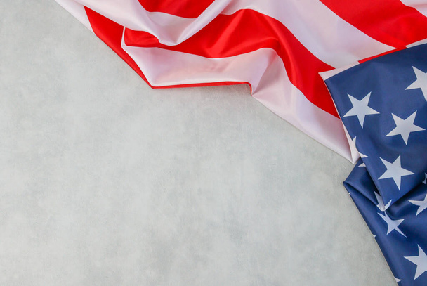 De Amerikaanse vlag ligt aan de rechterkant tegen een cementachtergrond met ruimte voor tekst aan de linkerkant, bovenaanzicht van dichtbij. - Foto, afbeelding