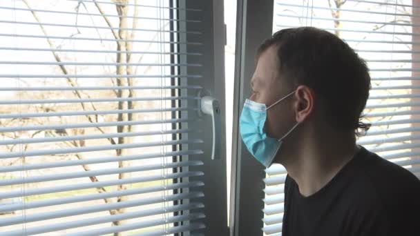 An einem sonnigen Tag steht ein Mann vor einem Fenster mit Jalousien und blickt traurig auf die Straße - Filmmaterial, Video
