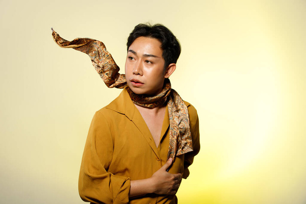 Half Body Portrait of 20s Asian LGBTQIA + Gay Mann schwarze Haare tragen gelbes Hemd mit Schal. Männermode posiert mit halbem Körper vor beigem Hintergrund - Foto, Bild